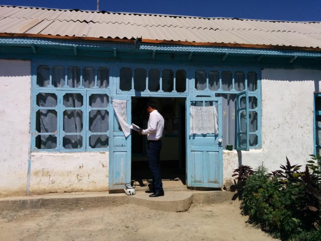 Photo of Habiba’s house with a loan officer at the entrance