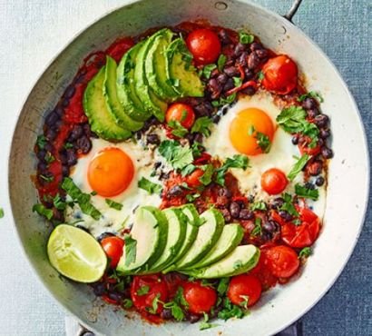 Sliced avocados, black beans and tomatoes with two fried eggs in a bowl