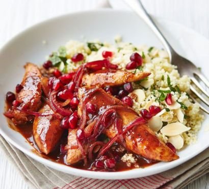 Plate of sliced cooked chicken breast covered in pomegranate sauce with couscous