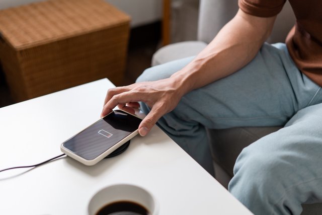 A person with his light blue jeans sitting on the couch and trying to charge his smartphone on the wireless battery charger.