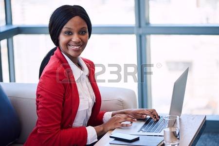 72483607-black-female-businesswoman-smiling-at-the-camera-while-seated-on-a-couch-in-a-business-lounge-with-h.jpg