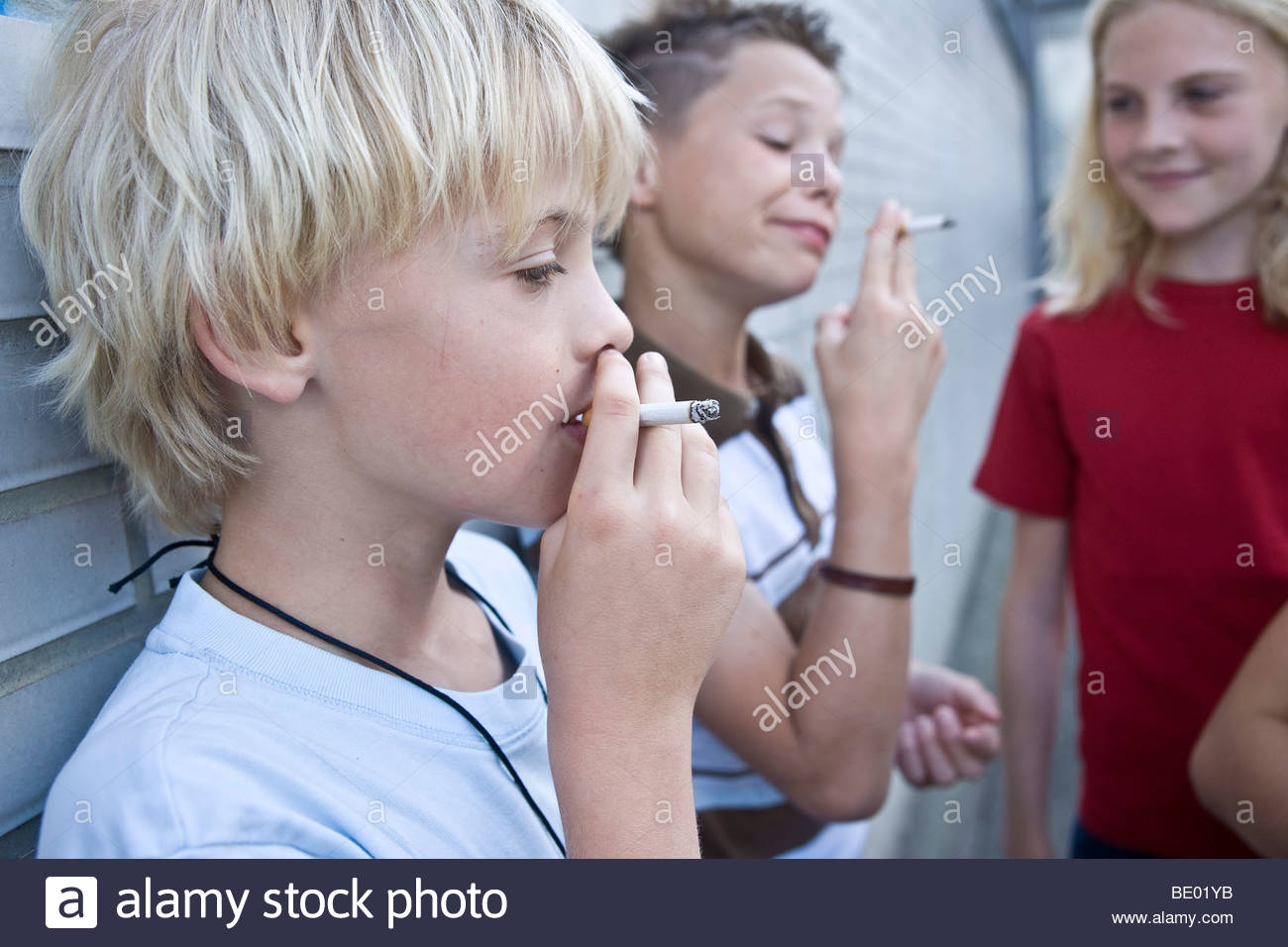two-young-boys-smoking-a-cigarette-a-girl-watching-BE01YB.jpg