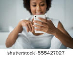 stock-photo-young-smiling-woman-sitting-on-the-bed-at-home-and-texting-with-her-smartphone-she-is-social-555427027.jpg