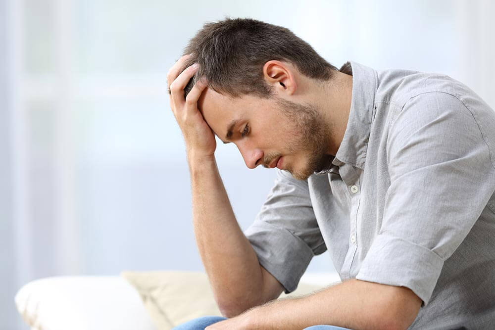 lighthousetreatment-7-ways-to-deal-with-anxiety-in-recovery-article-photo-of-side-view-of-a-sad-man-with-a-hand-on-the-head-sitting-on-a-couch-in-the-living-room-at-home-457511662.jpg
