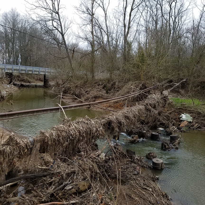 Abandoned railroad tracks hanging over creek with highway bridge in background