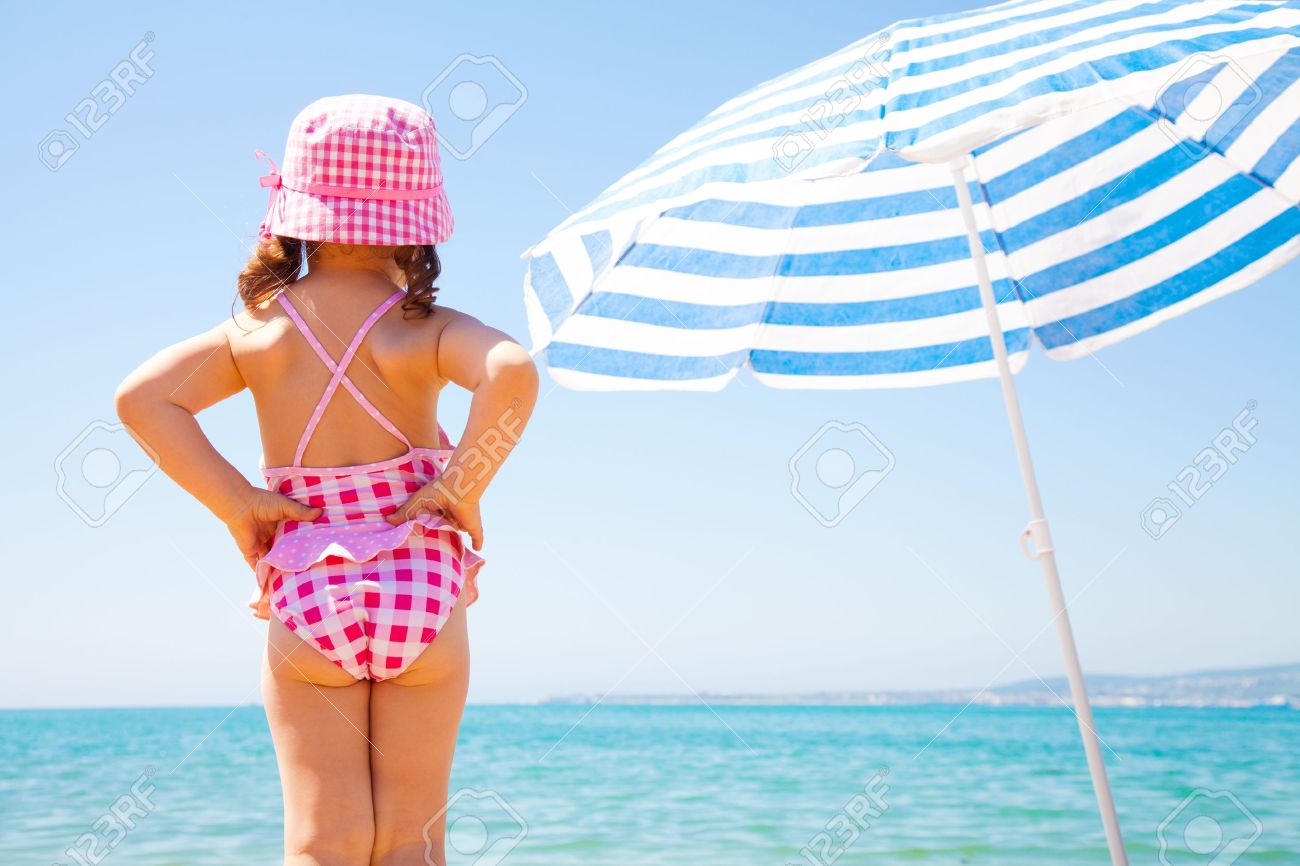14466355-the-little-girl-looks-at-the-sea-near-a-beach-umbrella-Stock-Photo.jpg