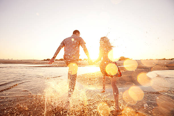 happy-couple-runs-through-waves-on-sunlit-beach-picture-id167408896.jpeg