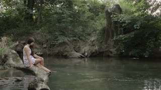girl-with-long-hair-sitting-on-a-log-and-wets-feet-in-the-water-of-the-river_vubucqsue__S0000.jpg