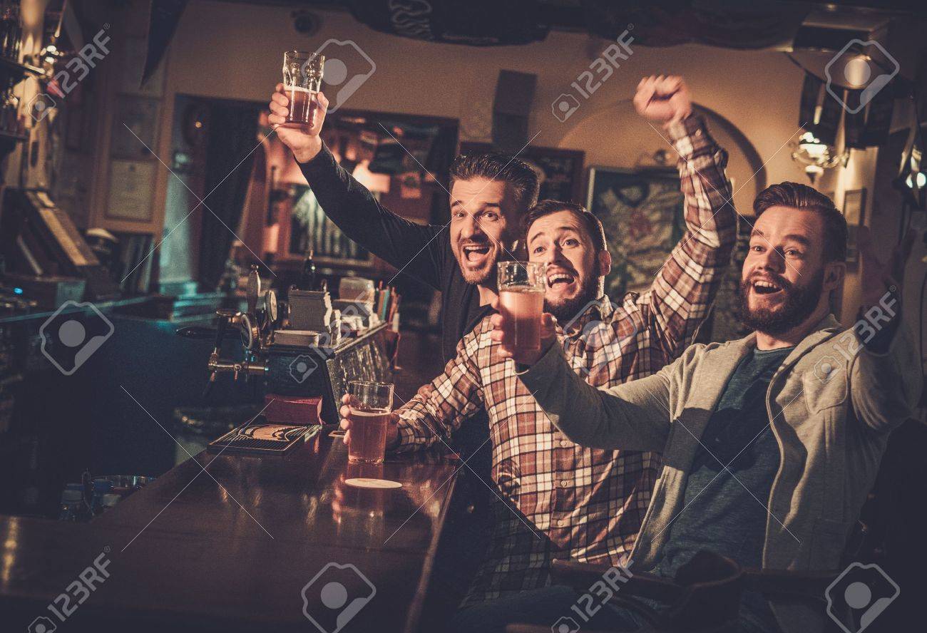 53766810-cheerful-old-friends-having-fun-watching-a-football-game-on-tv-and-drinking-draft-beer-at-bar-counte.jpg