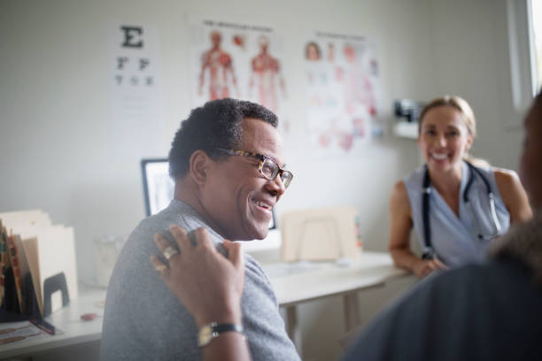 smiling-senior-man-talking-with-wife-and-doctor-in-examination-room-picture-id915090424.jpg