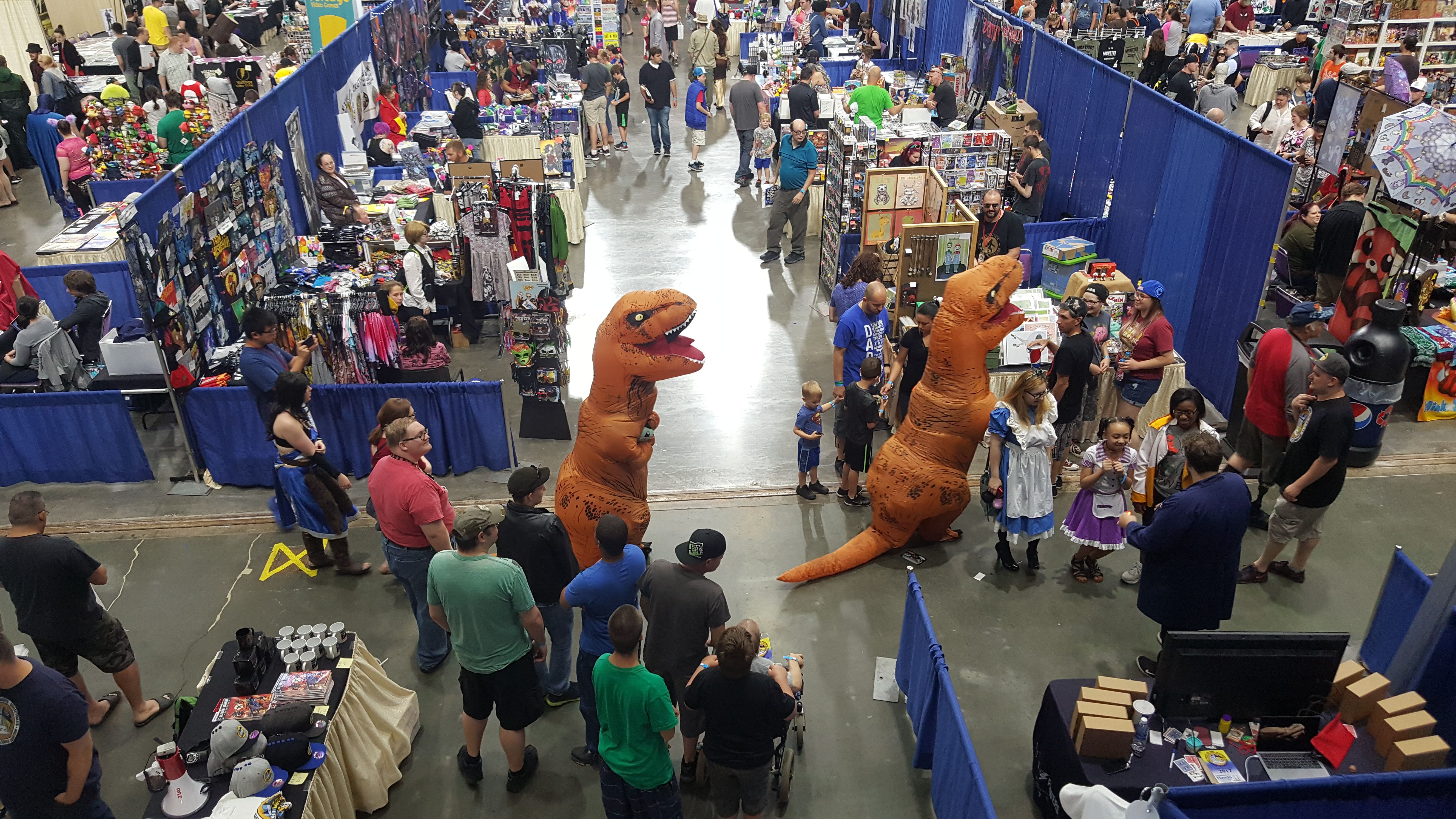 Two dinosaurs walk through the vendor floor at Salt City Comic Con